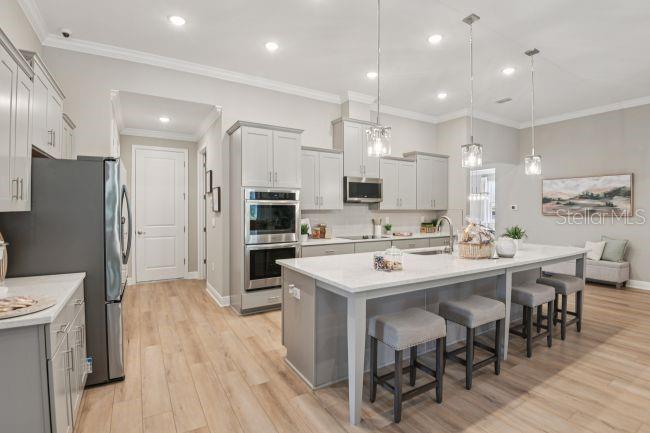 A modern kitchen features light gray cabinetry, a large white island with stools, and stainless appliances — 20 FERNON DRIVE, PALM COAST, FL