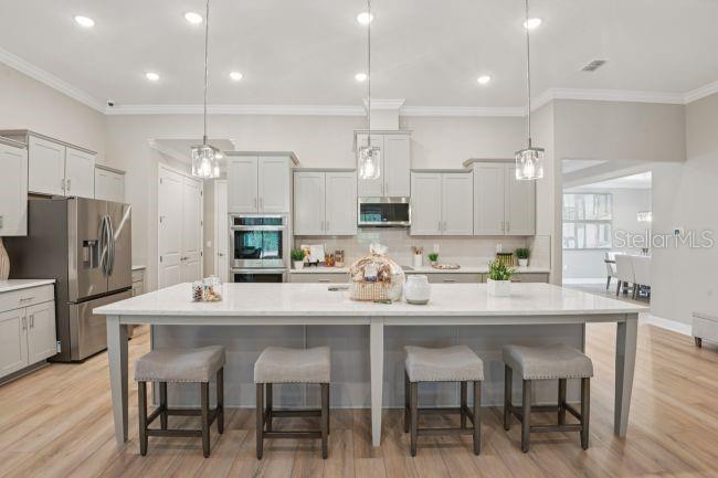 A modern kitchen features light gray cabinetry, a large white island with four stools, and stainless-steel appliances — 20 FERNON DRIVE, PALM COAST, FL