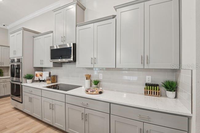 A modern kitchen features light gray cabinets, white countertops, stainless steel appliances, and a tiled backsplash — 20 FERNON DRIVE, PALM COAST, FL