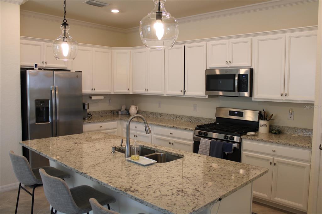 A kitchen features white cabinets, granite countertops, stainless steel appliances, and a large center island — 6647 CLAIRBORNE LANE, BRADENTON, FL