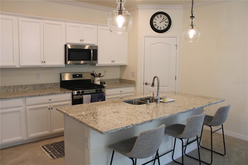 A kitchen features white cabinets, granite countertops, a center island with seating, and stainless appliances — 6647 CLAIRBORNE LANE, BRADENTON, FL