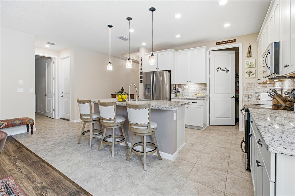 A kitchen features white cabinets, granite countertops, a center island with three stools, and tile flooring — 762 RUSTIC MILL DRIVE, ST AUGUSTINE, FL