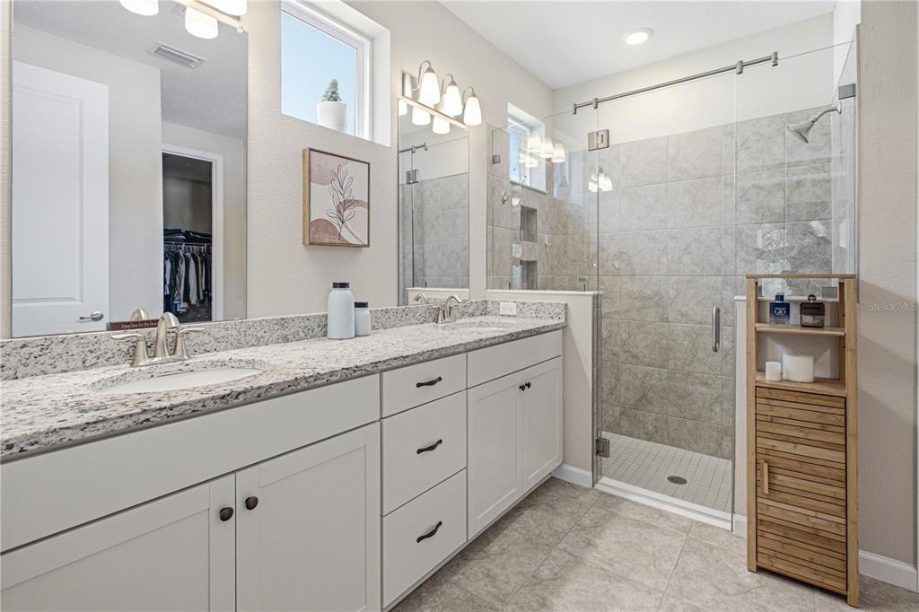 A bathroom features a double vanity with granite countertops, white cabinets, and a glass-enclosed shower — 762 RUSTIC MILL DRIVE, ST AUGUSTINE, FL