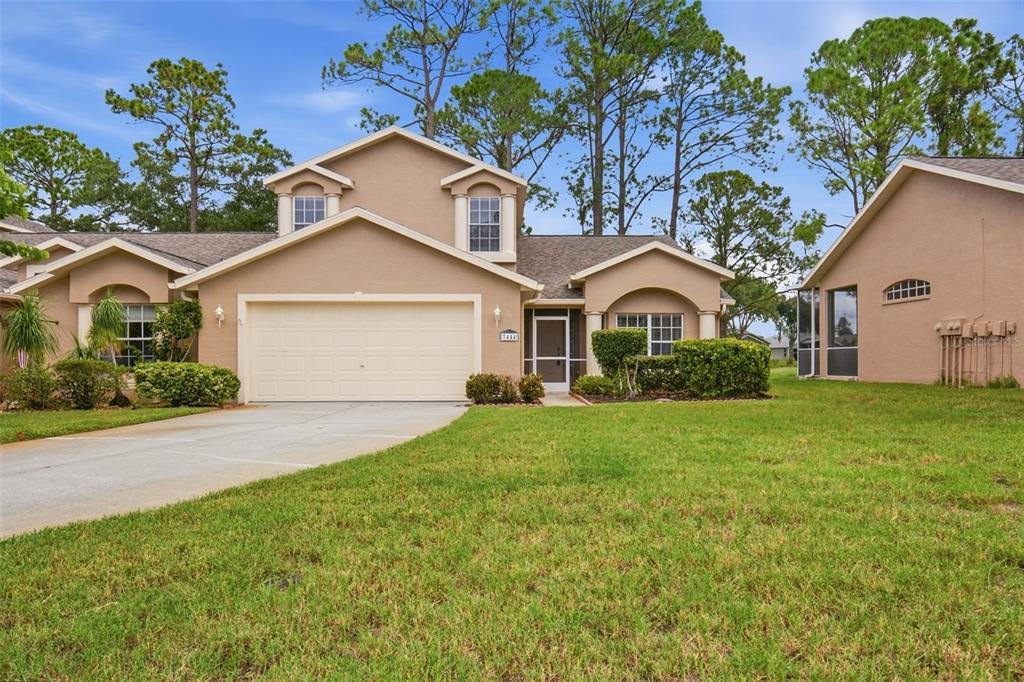 A two-story tan house with a two-car garage and a front lawn — 7444 MOORGATE COURT, NEW PORT RICHEY, FL