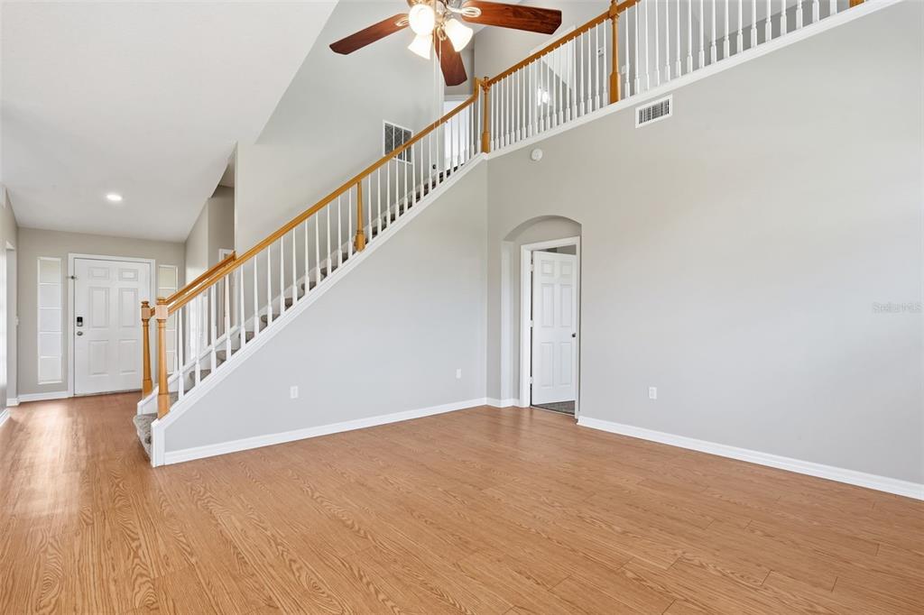 A bright living room features light wood flooring, a staircase with white railings, and high ceilings — 7444 MOORGATE COURT, NEW PORT RICHEY, FL