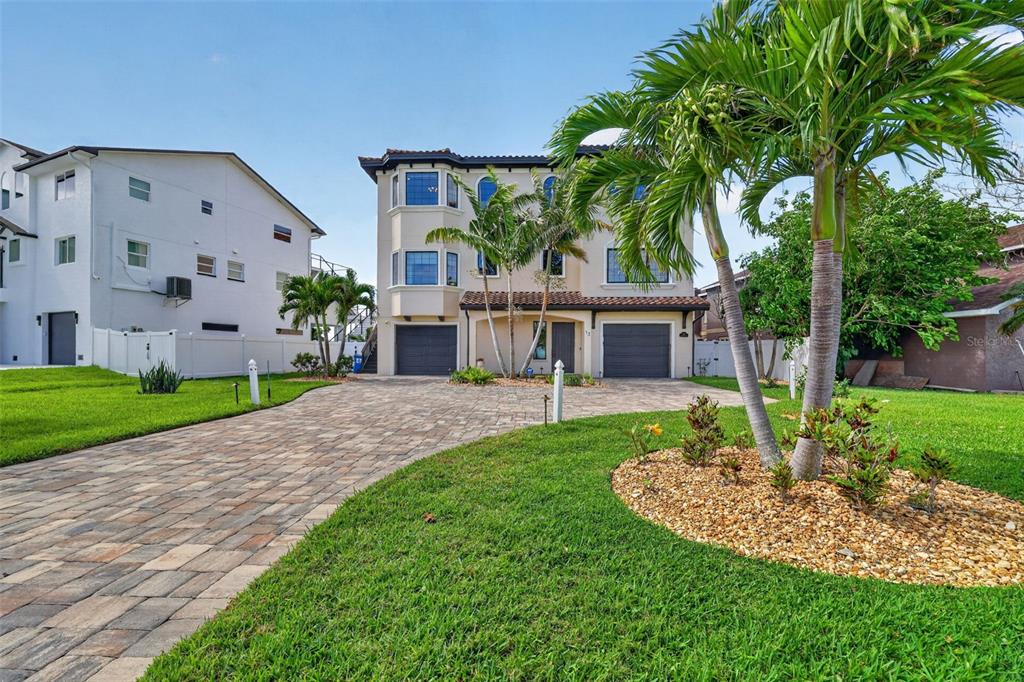 A three-story house with a paved driveway, two garages, and palm trees in the front yard — 13 TREASURE LN, TREASURE ISLAND, FL