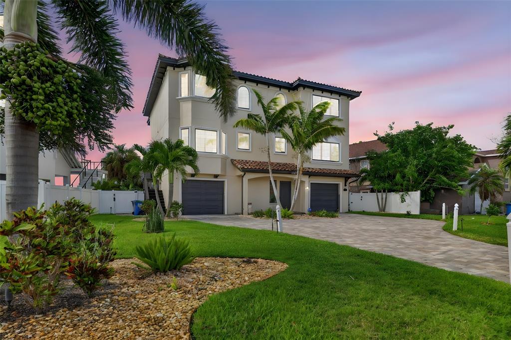 A three-story house with two garages, a paved driveway, and palm trees at sunset — 13 TREASURE LN, TREASURE ISLAND, FL