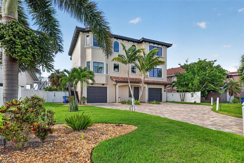 A three-story beige house with two garages, a paved driveway, and palm trees — 13 TREASURE LN, TREASURE ISLAND, FL