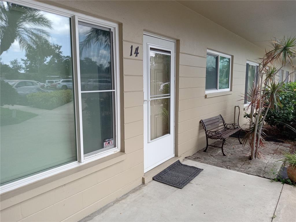 The exterior of a ground-level apartment unit features a front door numbered 14 and a bench — 2464 AUSTRALIA WAY E UNIT 14, CLEARWATER, FL