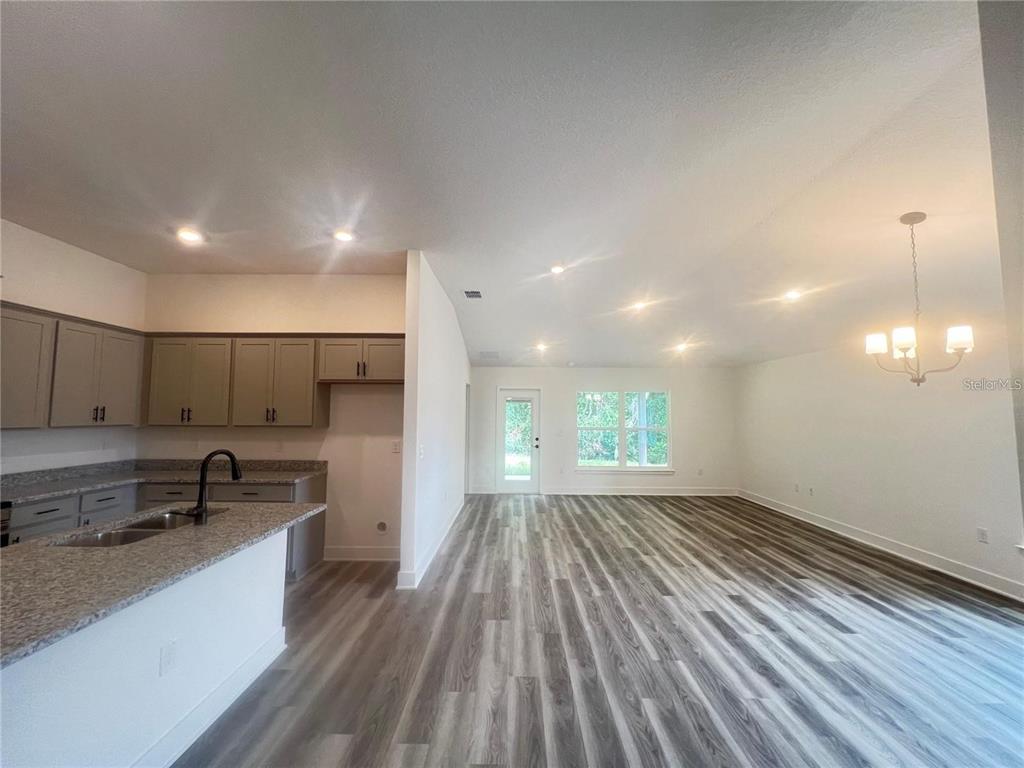 An open-concept kitchen and living area features gray cabinets, granite countertops, and wood-look flooring — 3648 LINDBERGH STREET, LAKELAND, FL