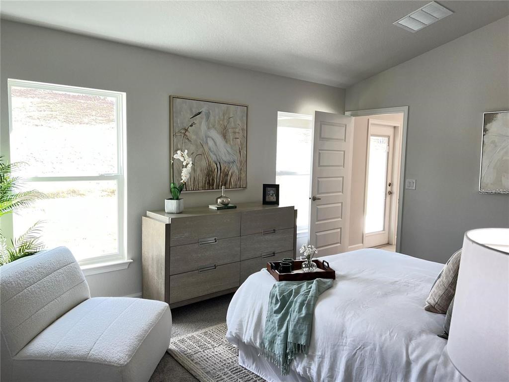 A bedroom features a bed, a dresser with artwork, a chair, and an open doorway — 3648 LINDBERGH STREET, LAKELAND, FL