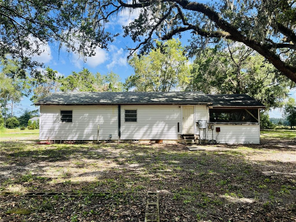 A white, single-story house with a screened-in porch sits on a dirt lot under trees — 3324 TAYLOR AVENUE, COLEMAN, FL