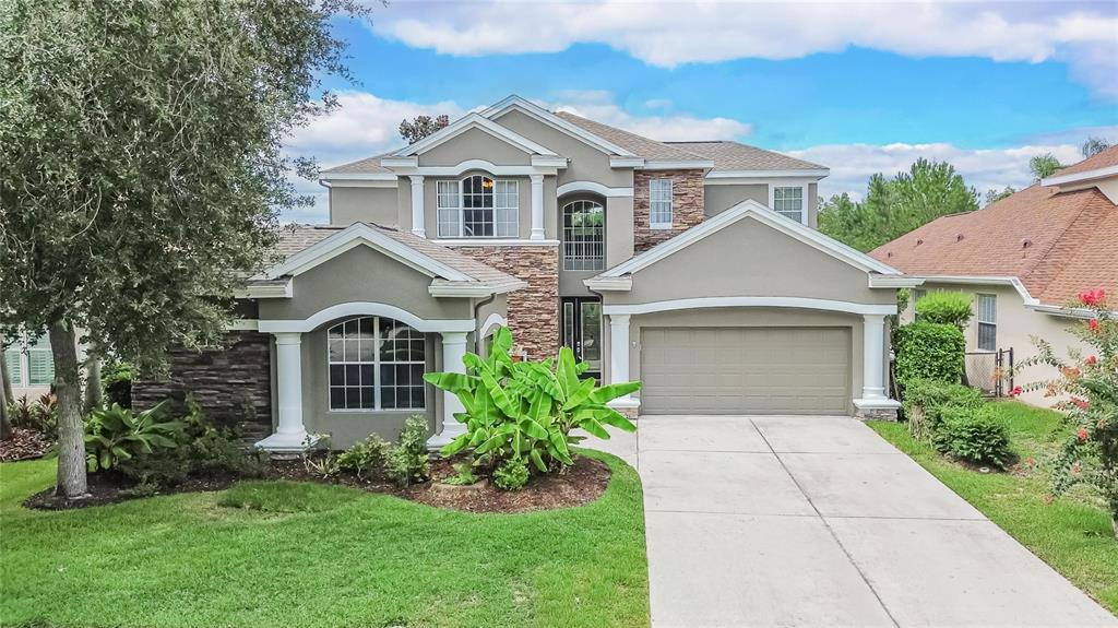 A two-story house with a gray stucco exterior, stone accents, and palm trees in front — 10103 DEERCLIFF DRIVE, TAMPA, FL