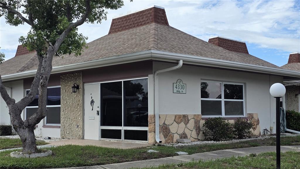 A single-story building with a brown shingled roof, stone accents, and a white front door — 4330 TAHITIAN GARDENS CIRCLE UNIT A, HOLIDAY, FL