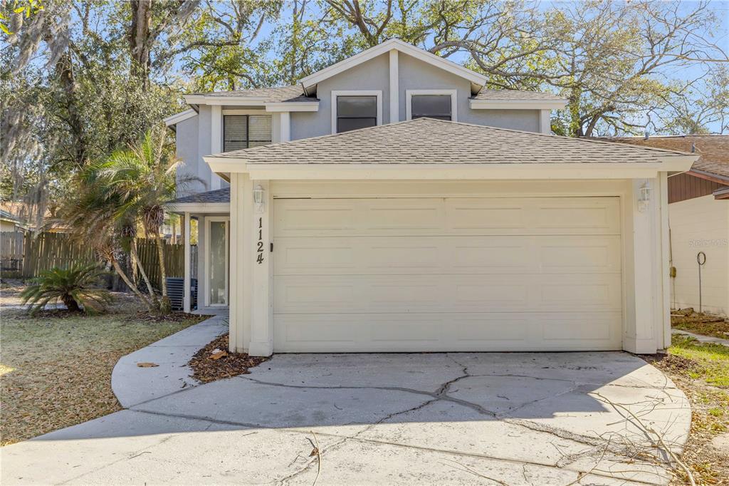 A two-story house with a beige garage, a concrete driveway, and surrounding trees — 1124 MILL RUN CIRCLE, APOPKA, FL