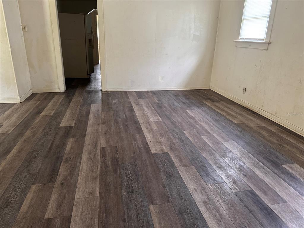 A living room features wood-look flooring, a gray sofa, a television console, and a white door — 1049 PLATEAU AVENUE, LAKELAND, FL