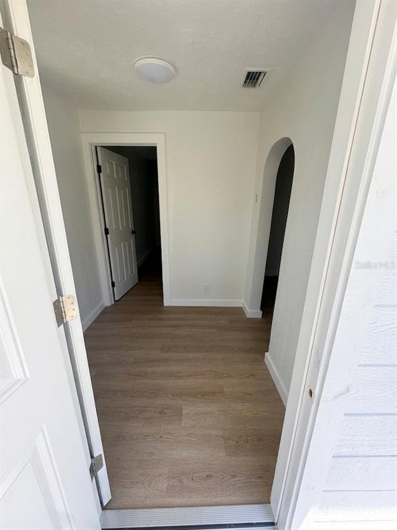An interior view shows a hallway with light wood-look flooring, a white door, and an archway — 1543 43RD STREET S UNIT B, ST PETERSBURG, FL