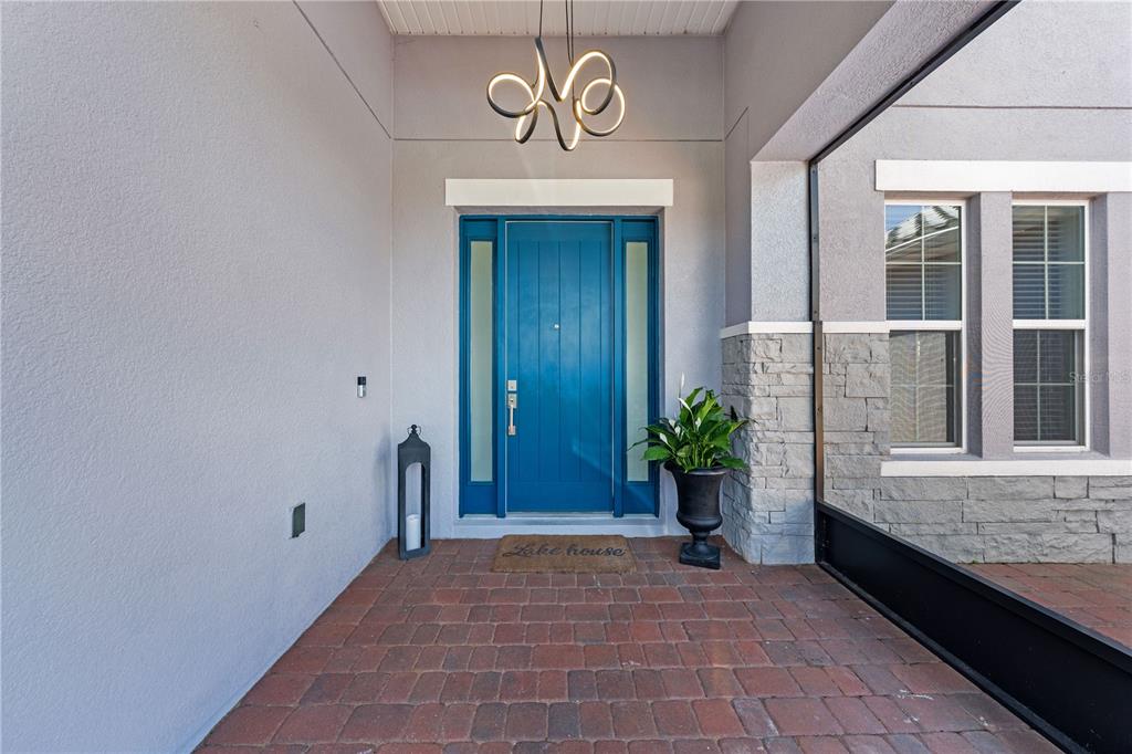 A blue front door with sidelights sits on a brick porch under a modern chandelier — 840 SPINNAKER WAY, KISSIMMEE, FL