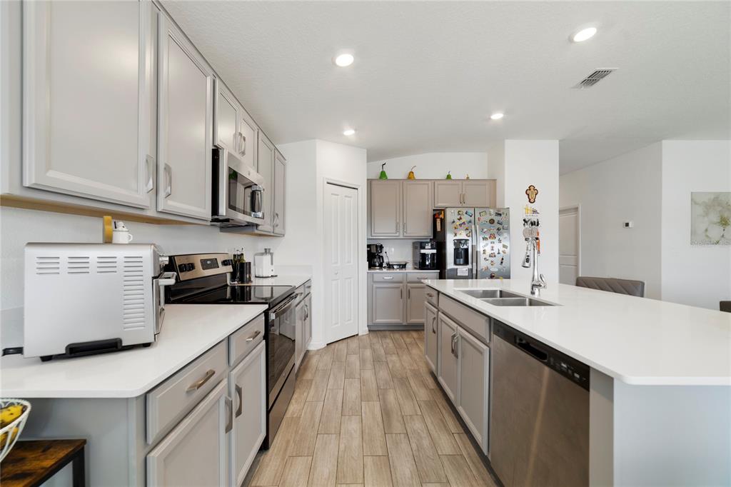 A kitchen features light gray cabinets, white countertops, stainless steel appliances, and wood-look tile flooring — 5270 PRESERVE BOULEVARD, ST CLOUD, FL