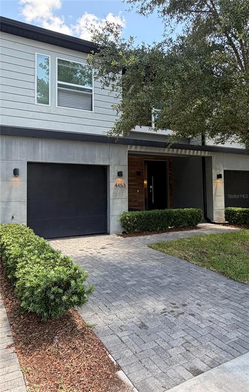 A two-story modern townhouse features a gray garage, wood-paneled entryway, and a paved driveway — 4453 LE REVE COURT, KISSIMMEE, FL