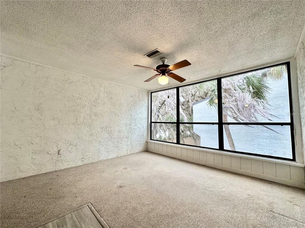 A sunroom with beige carpeting, textured walls, a ceiling fan, and large windows overlooking trees — 2834 SW 14TH DRIVE UNIT 305, GAINESVILLE, FL