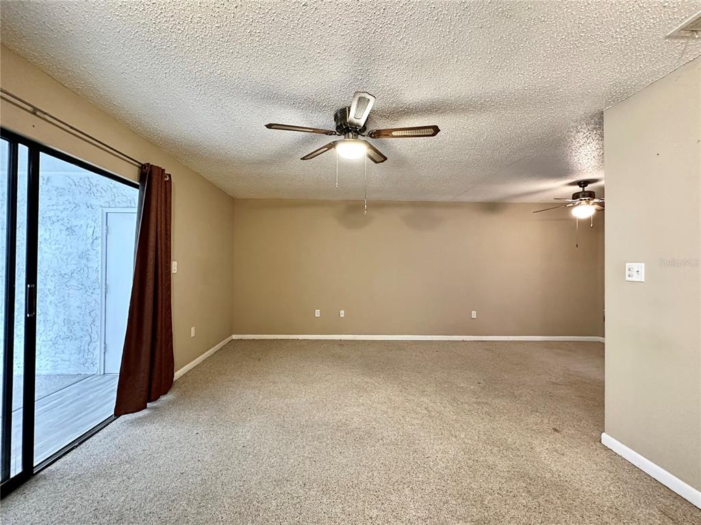 A carpeted living room features a ceiling fan, beige walls, and sliding glass patio doors — 2834 SW 14TH DRIVE UNIT 305, GAINESVILLE, FL