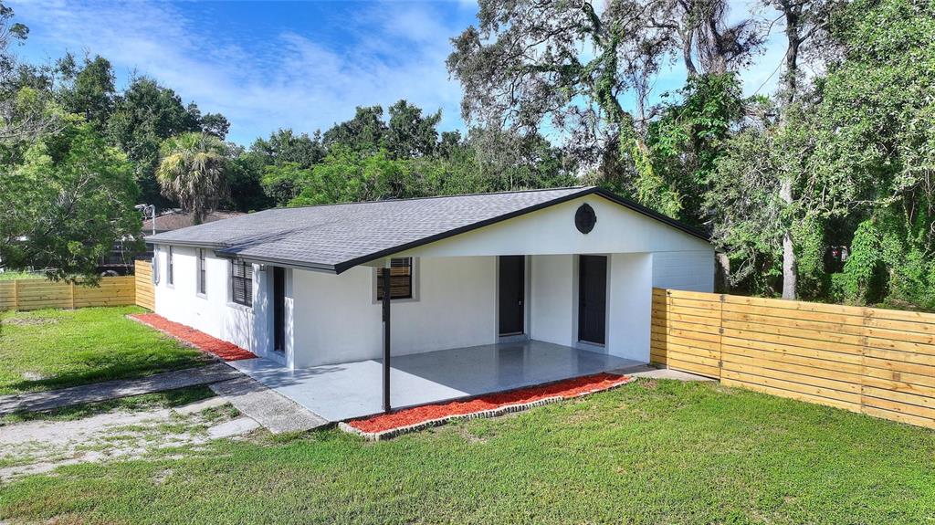 A white single-story house features a covered front porch, dark trim, and a wooden fence — 10020 N 10TH STREET, TAMPA, FL