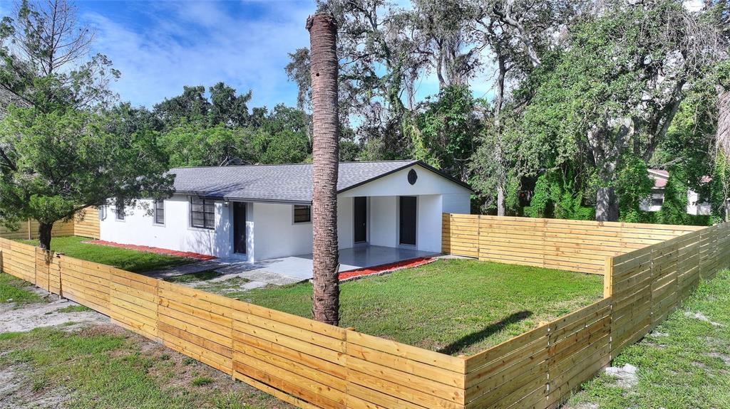 A white single-story house with a grey roof and a wooden fence enclosing the yard — 10020 N 10TH STREET, TAMPA, FL