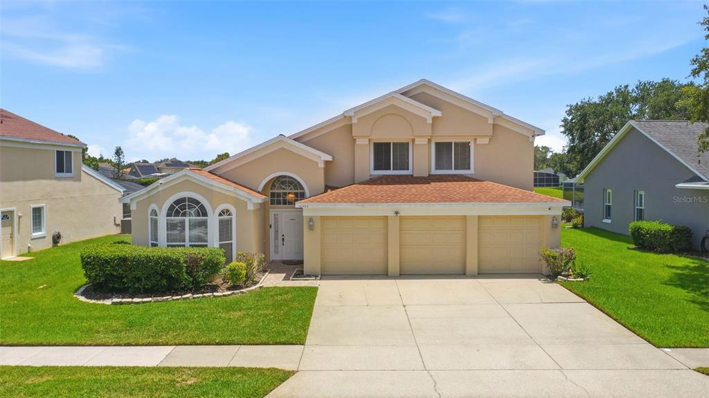 An exterior view of a two-story tan house with a three-car garage and lawn — 13494 FALCON POINTE DRIVE, ORLANDO, FL
