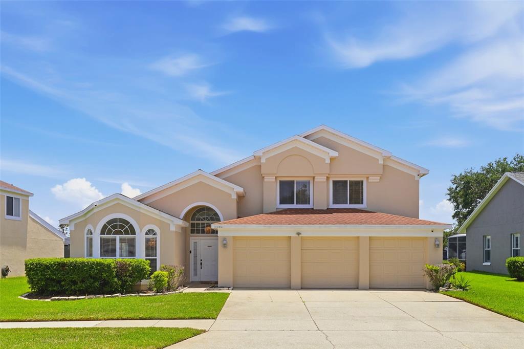 A two-story suburban house with a beige stucco exterior, a three-car garage, and a driveway — 13494 FALCON POINTE DRIVE, ORLANDO, FL