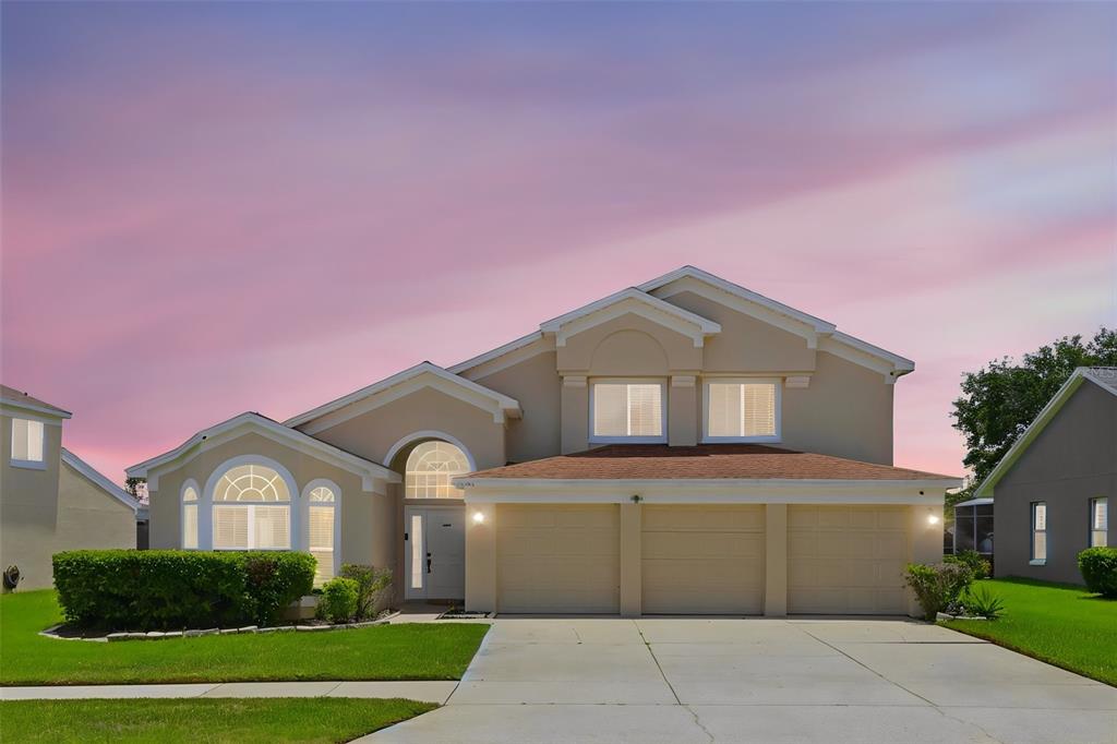 A two-story suburban house with a three-car garage and a concrete driveway at sunset — 13494 FALCON POINTE DRIVE, ORLANDO, FL