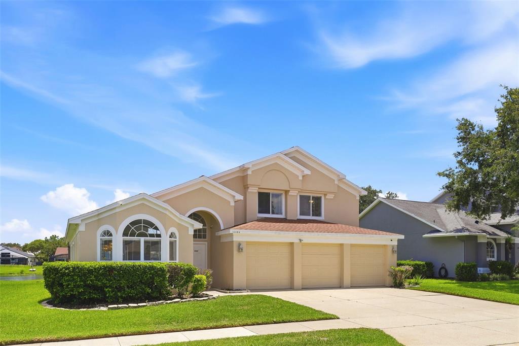 A two-story beige house with a three-car garage and a front lawn under blue skies — 13494 FALCON POINTE DRIVE, ORLANDO, FL