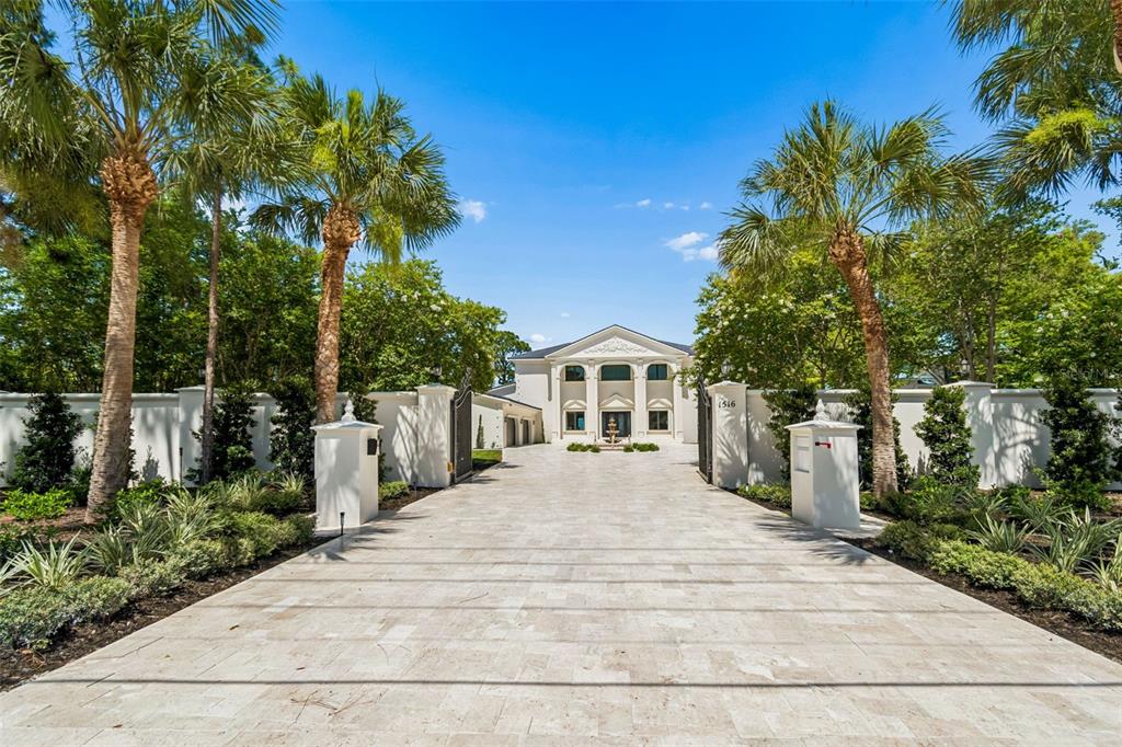 A paved driveway leads to a white two-story mansion framed by palm trees and walls — 1516 BAYSHORE BOULEVARD, DUNEDIN, FL
