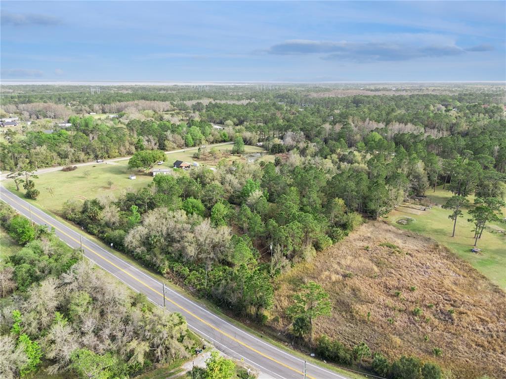 An aerial view shows a paved road running alongside a wooded lot and open fields — 541 E OSCEOLA ROAD, GENEVA, FL