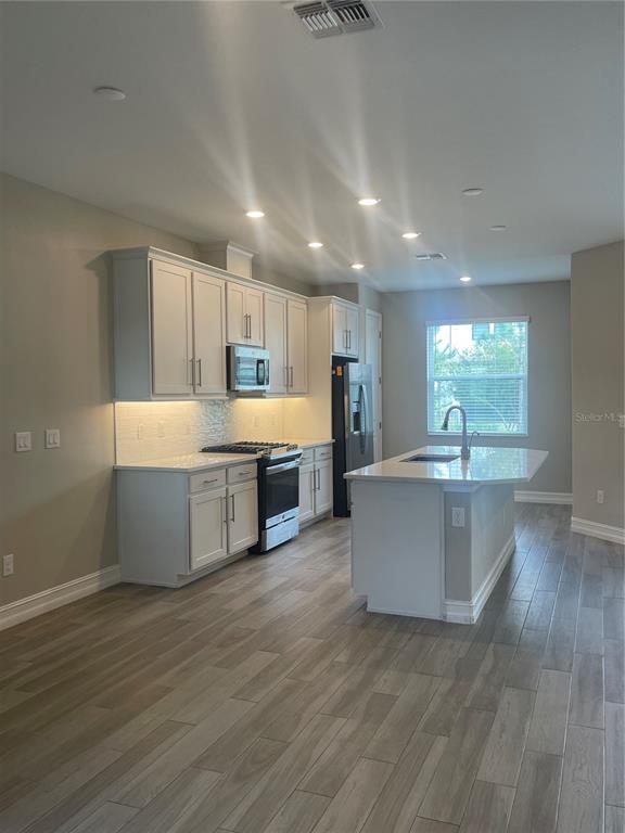 An open-concept kitchen features white cabinetry, a center island, and light wood-look tile flooring — 4596 ALMADA LANE, WESLEY CHAPEL, FL