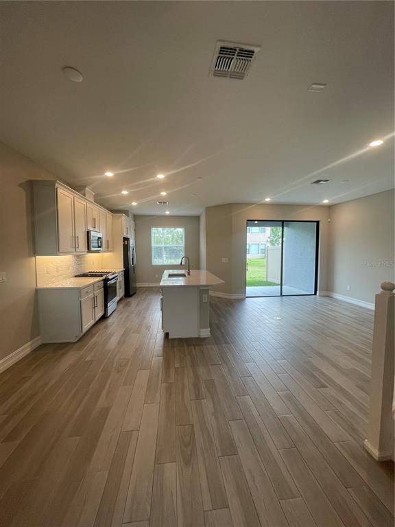 A modern kitchen features white cabinets, stainless steel appliances, a center island, and wood-look flooring — 4596 ALMADA LANE, WESLEY CHAPEL, FL