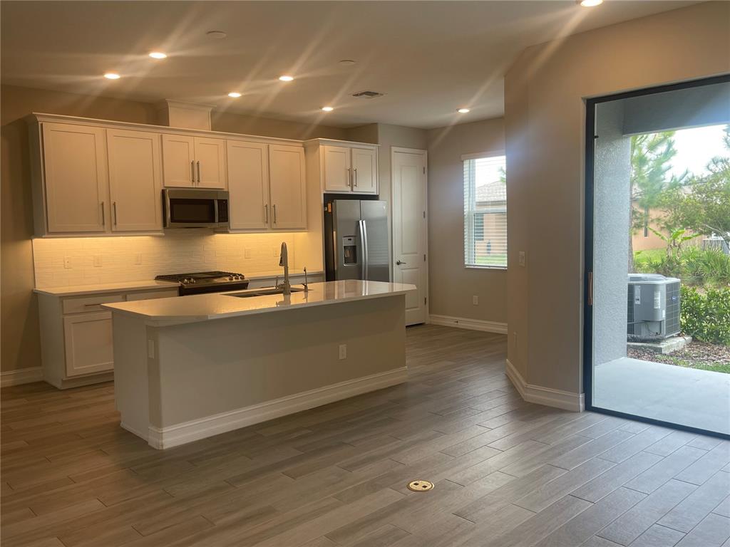 A kitchen features white cabinets, a central island with a sink, and light wood-look flooring — 4596 ALMADA LANE, WESLEY CHAPEL, FL