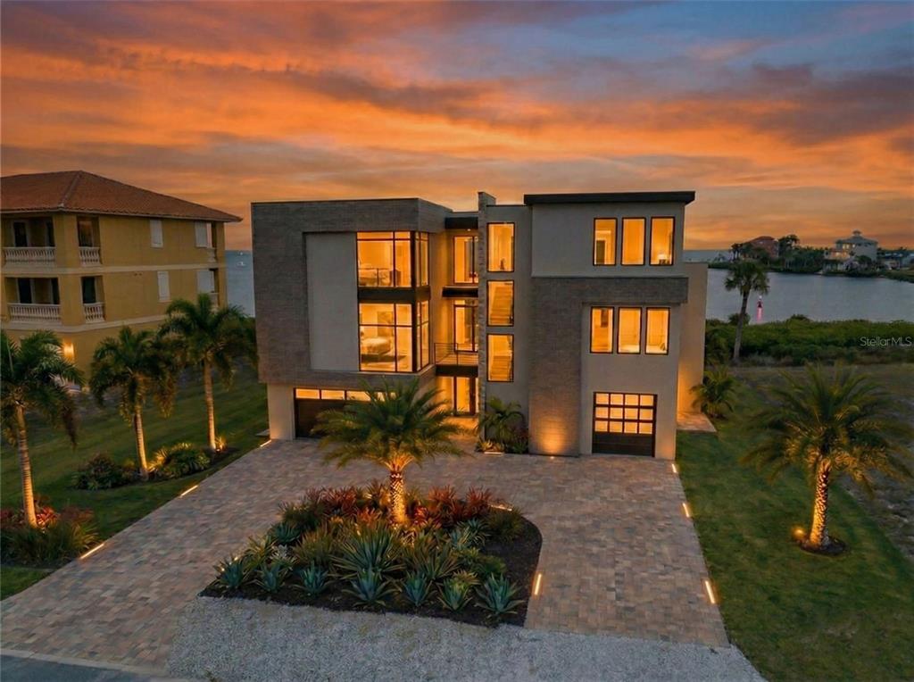 A modern multi-story house with a paved driveway and palm trees at sunset — 25 HARBORPOINTE DRIVE, PORT RICHEY, FL
