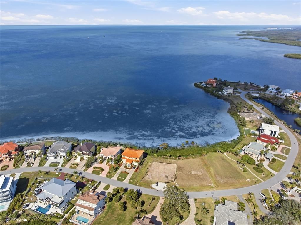 An aerial view shows waterfront homes and vacant lots along a curved coastal road — 25 HARBORPOINTE DRIVE, PORT RICHEY, FL
