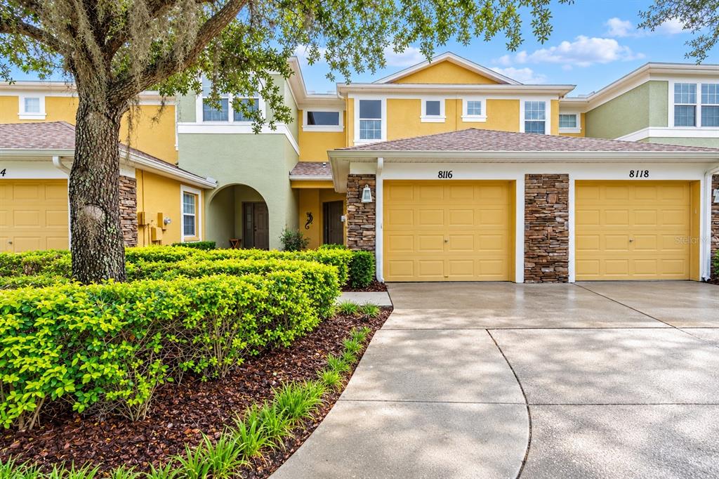 A two-story house exterior features yellow and green stucco walls, stone accents, and a garage — 8116 STONE PATH WAY, TAMPA, FL