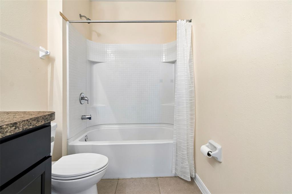 A bathroom features a white tiled tub-shower combo, a toilet, and a dark vanity — 11181 LELAND GROVES DRIVE, RIVERVIEW, FL