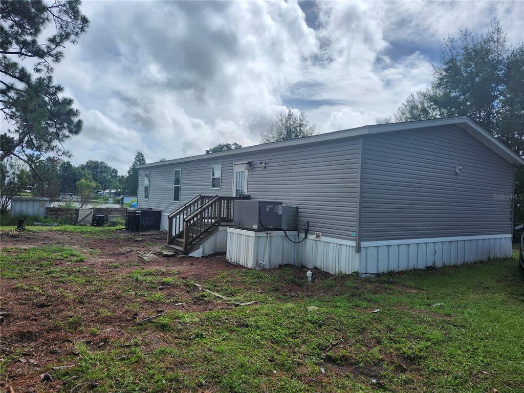 A gray-sided mobile home features a wooden staircase and white skirting on a grassy lot — 4550 POLK CITY ROAD, HAINES CITY, FL