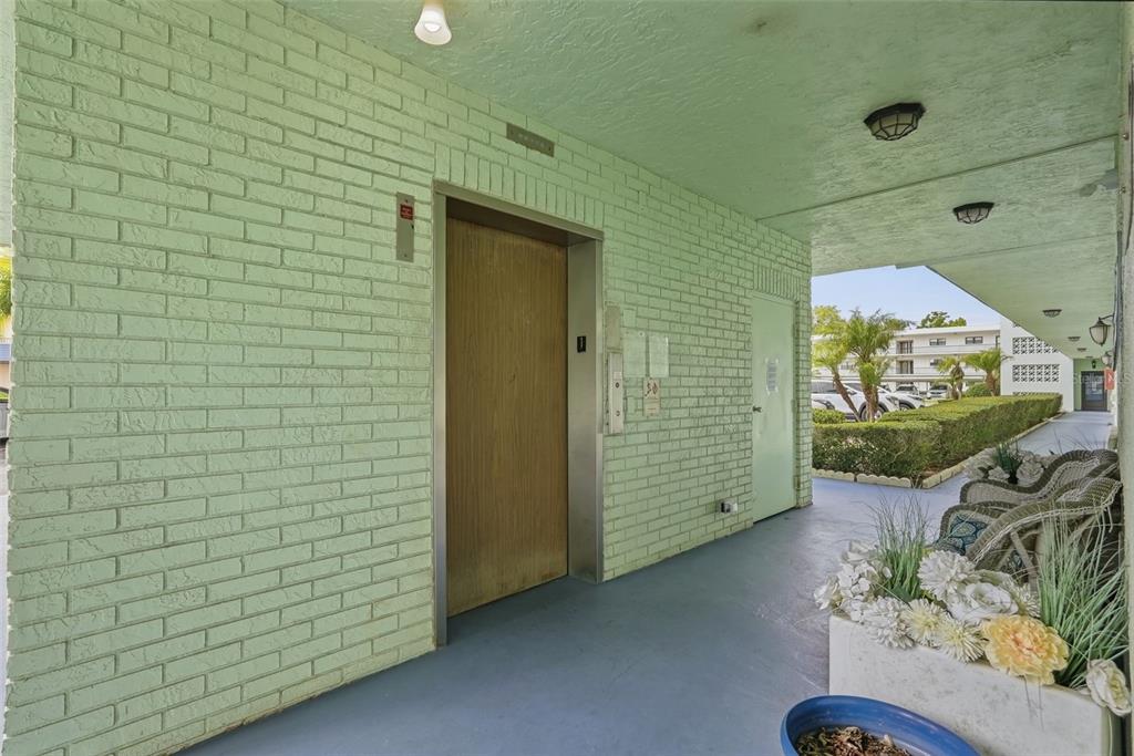 An outdoor walkway features a light green brick wall, an elevator, and a seating area — 5973 TERRACE PARK DRIVE N UNIT 109, ST PETERSBURG, FL