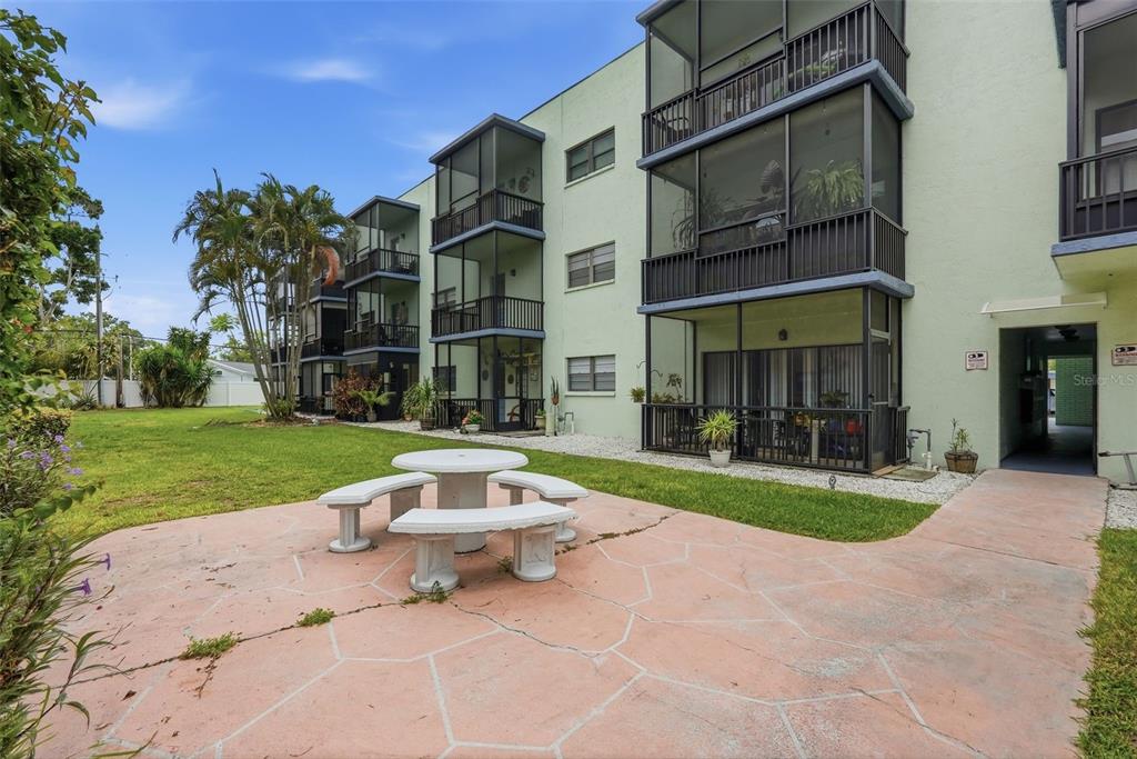 A concrete patio with a stone table sits outside a multi-story apartment building — 5973 TERRACE PARK DRIVE N UNIT 109, ST PETERSBURG, FL