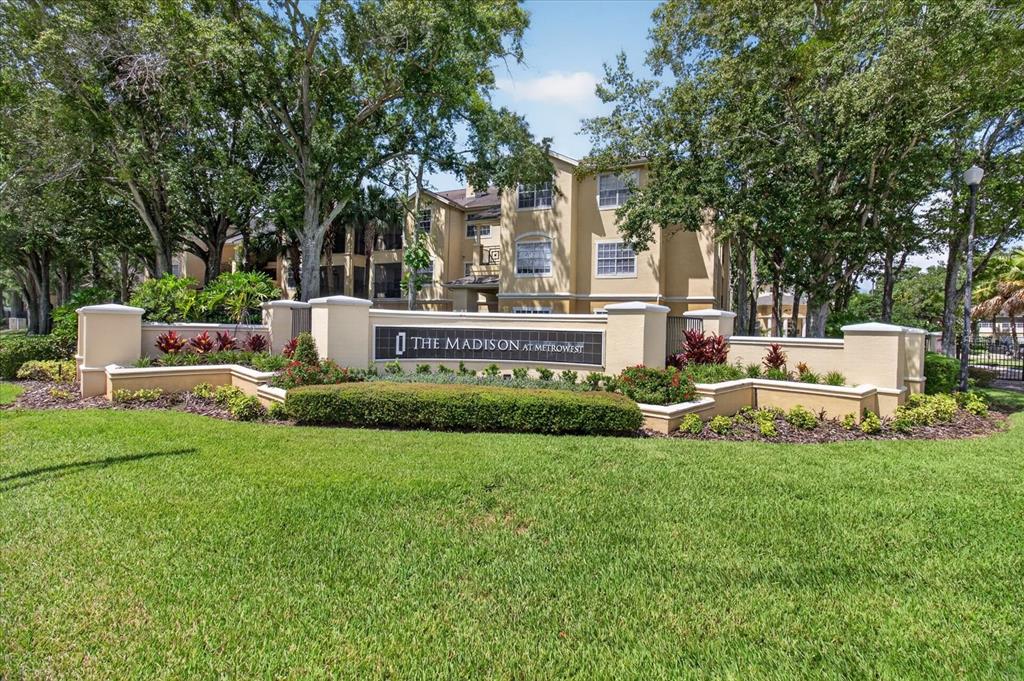 A beige apartment building stands behind a stone monument sign surrounded by landscaping and trees — 2612 ROBERT TRENT JONES DRIVE UNIT 711, ORLANDO, FL