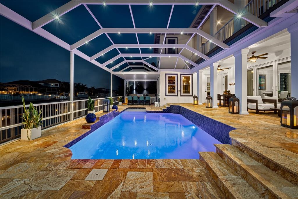 A screened-in pool area with stone decking, a waterfall feature, and outdoor seating at night — 713 ISLEBAY DRIVE, APOLLO BEACH, FL