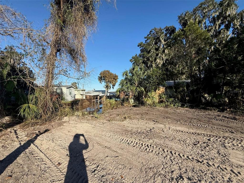 A muddy, unpaved lot with tire tracks leads toward houses and trees under a clear sky — 748 CR 477A, LAKE PANASOFFKEE, FL