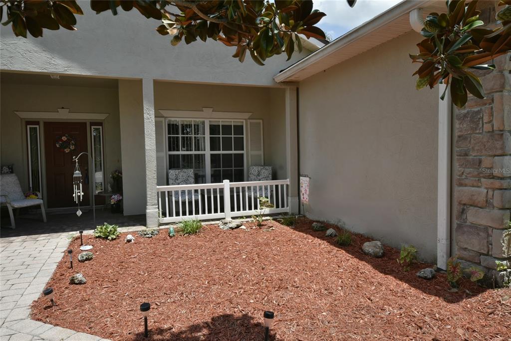 A front porch with a white railing sits beside a mulched garden bed and walkway — 4360 ASHTON CLUB DRIVE, LAKE WALES, FL