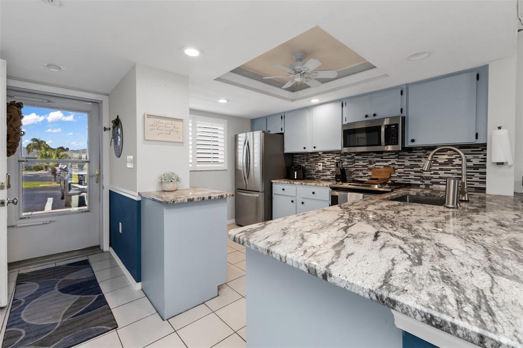 A kitchen features light blue cabinets, granite countertops, stainless steel appliances, and a tiled floor — 12274 SW EGRET CIRCLE UNIT 3302, LAKE SUZY, FL