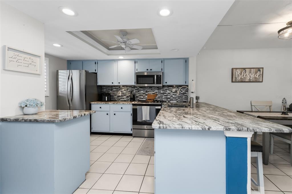 A kitchen features light blue cabinets, granite countertops, stainless steel appliances, and a tiled floor — 12274 SW EGRET CIRCLE UNIT 3302, LAKE SUZY, FL